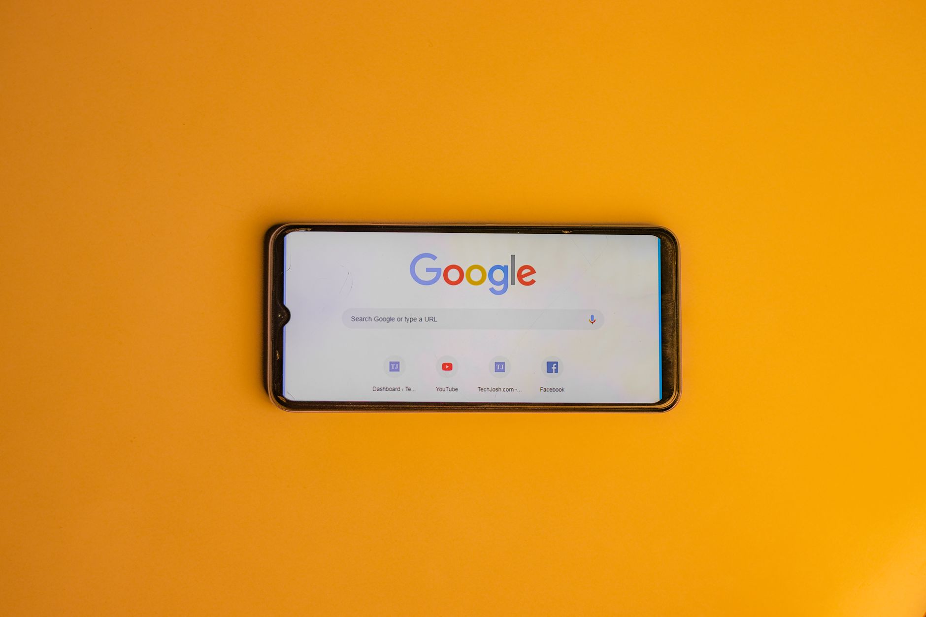 Smartphone displaying Google search page on a vibrant yellow background.