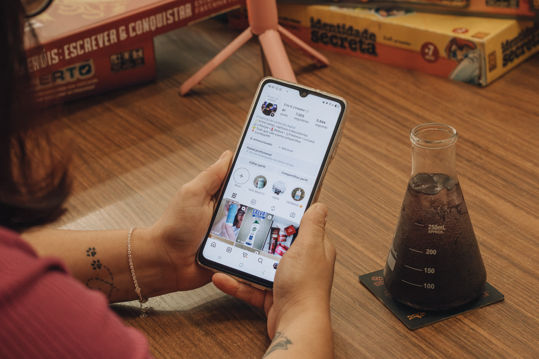 Close-up of hands holding a smartphone with a beaker drink nearby.